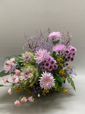 Artistic side flower basket arrangement in purple and yellow tones