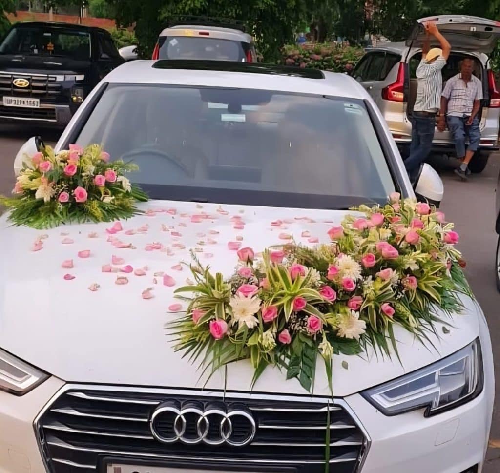 white car decorated with pink roses, white chrysanthemums, lilies, and fresh green foliage on the bonnet, designed for wedding celebrations
