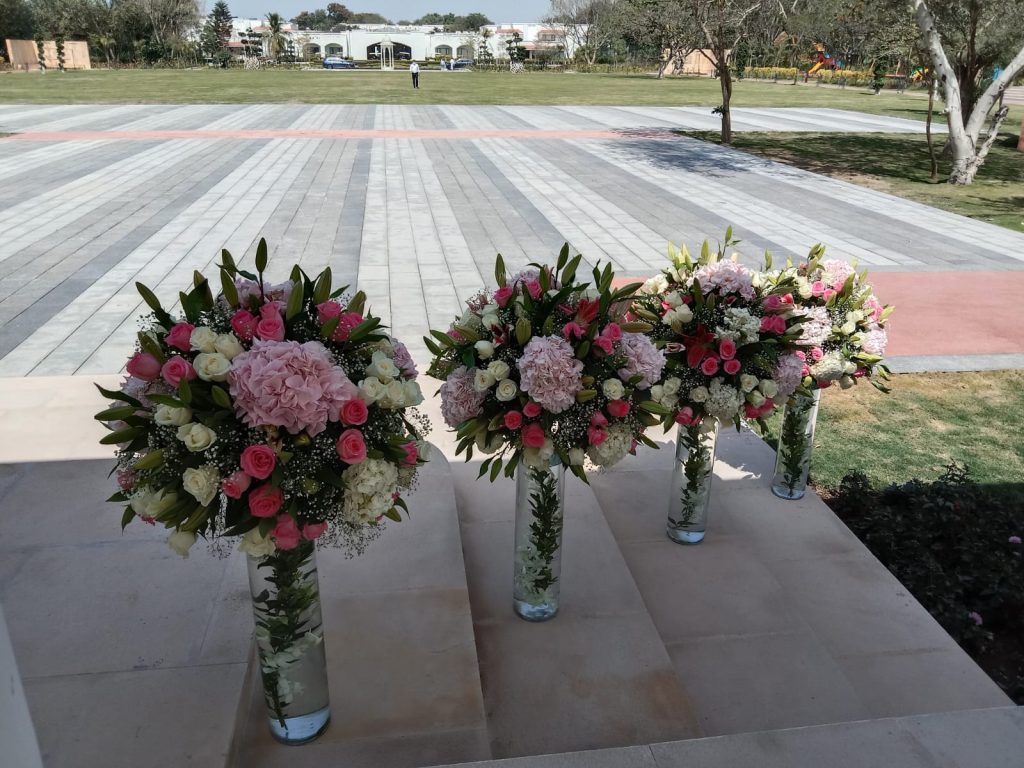 Luxury floral stand arrangements featuring pink hydrangeas, pink roses, white roses, lilies, baby’s breath, and fresh greenery in glass vases for wedding aisle or entrance décor.