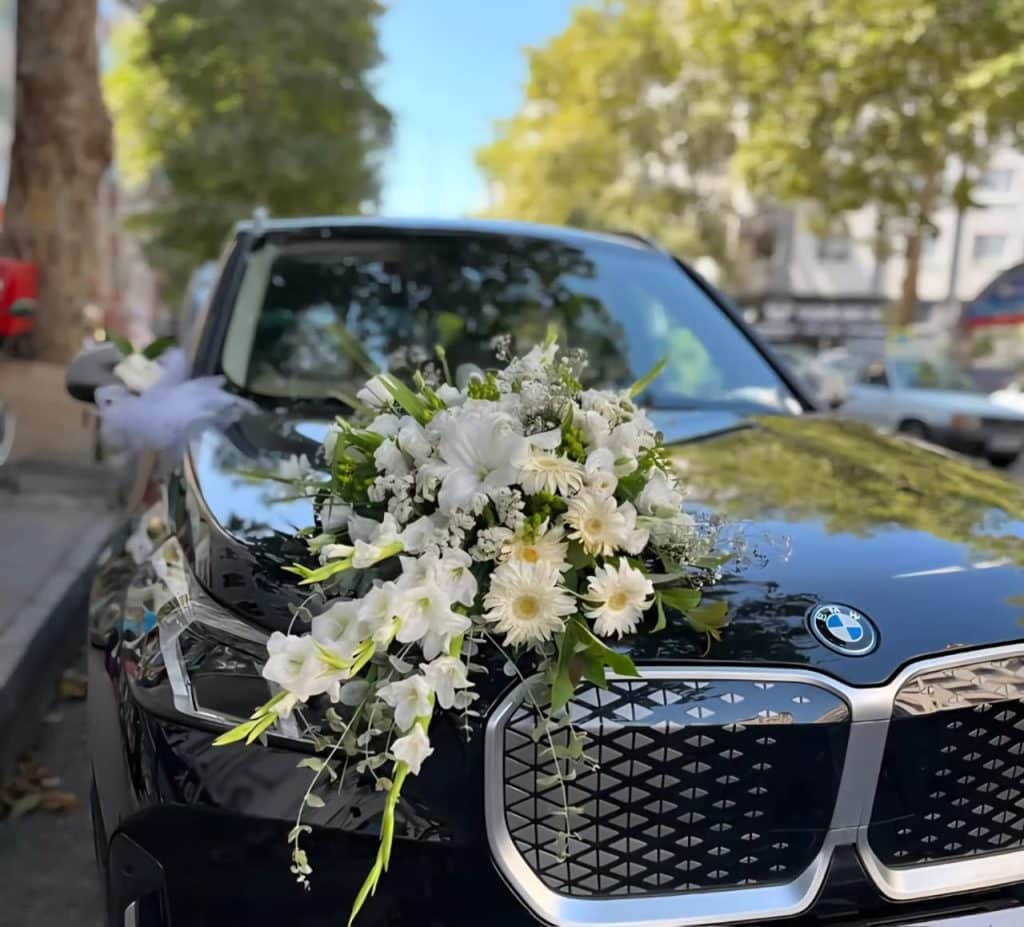 Elegant wedding car decoration featuring white lilies, white gerberas, baby’s breath, and fresh greenery arranged on the bonnet of a luxury black BMW in Mumbai.