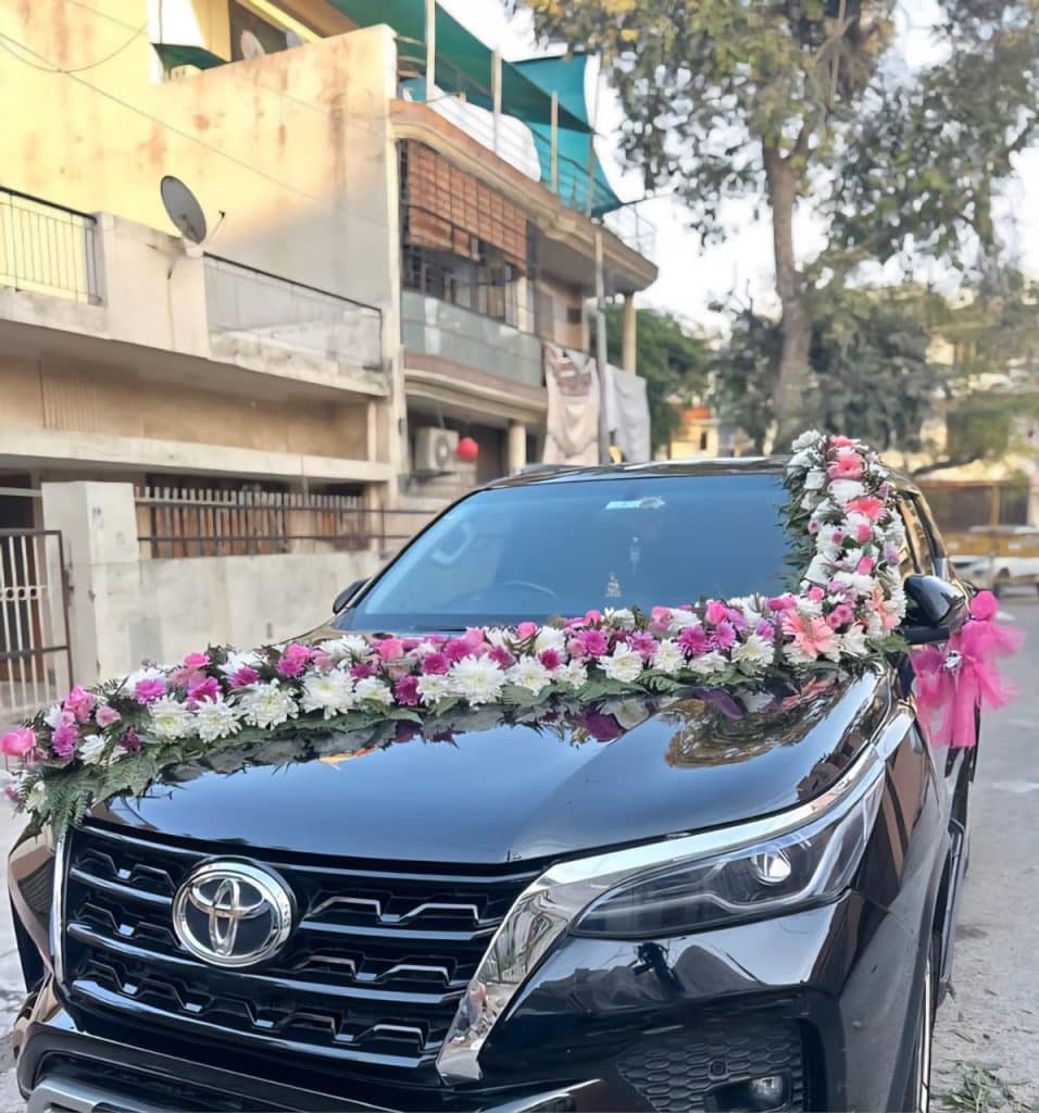 Stylish car decoration with fresh pink and white chrysanthemums, daisy flowers, and greenery arranged across the bonnet and side mirror for wedding celebrations in Mumbai.
