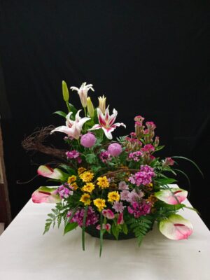 Colorful floral basket arrangement with white oriental lilies, pink anthuriums, yellow chrysanthemums, globe flowers, and seasonal fillers