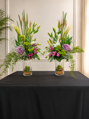 fresh flower arrangement featuring white lilies, calla lilies, ornamental cabbage, green button chrysanthemums, pink dianthus flowers, baby's breath, wheat stems, and lush greenery in a tall clear glass vase.left and right