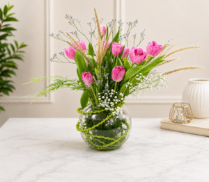 Fresh pink tulip flower arrangement with baby’s breath, limonium and decorative grass in a round glass vase