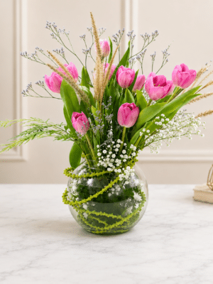 Fresh pink tulip flower arrangement with baby’s breath, limonium and decorative grass in a round glass vase