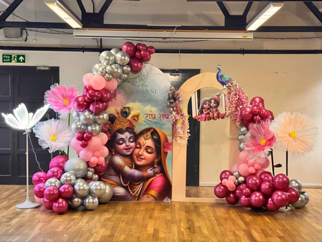 Krishna-themed baby shower decoration with a pink and silver balloon arch and Krishna Yashoda backdrop