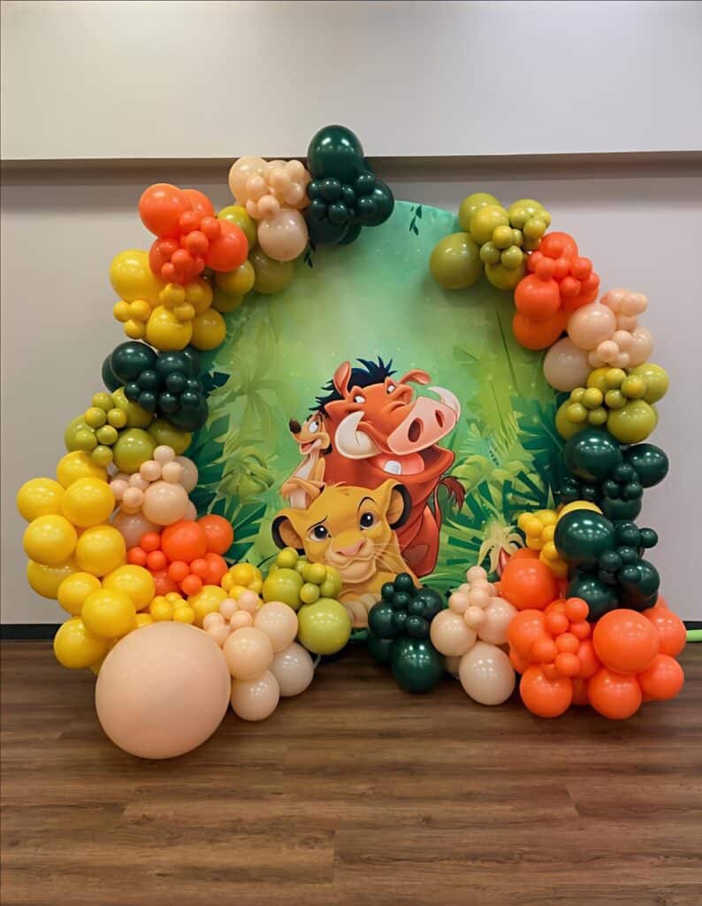 Lion King-themed birthday decoration with colourful balloon arch and jungle animal backdrop
