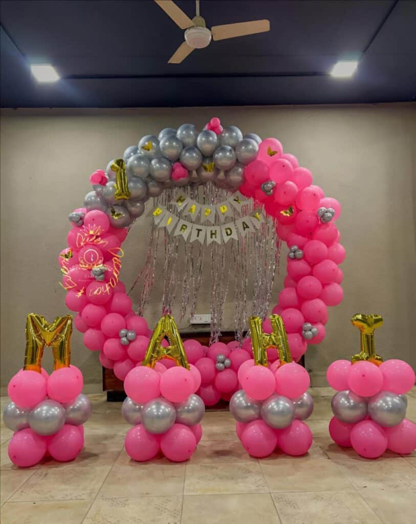 Pink and silver birthday balloon arch with a 'Happy Birthday' banner and balloon letters