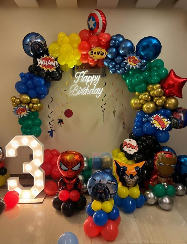 Superhero-themed birthday decoration with colourful balloon arch, superhero characters and number 3